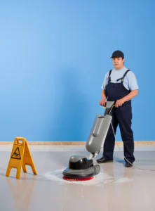 עובד ניקיון משתמש במכונת פוליש על רצפה מבריקה, עם תמרור אזהרה לציבור.